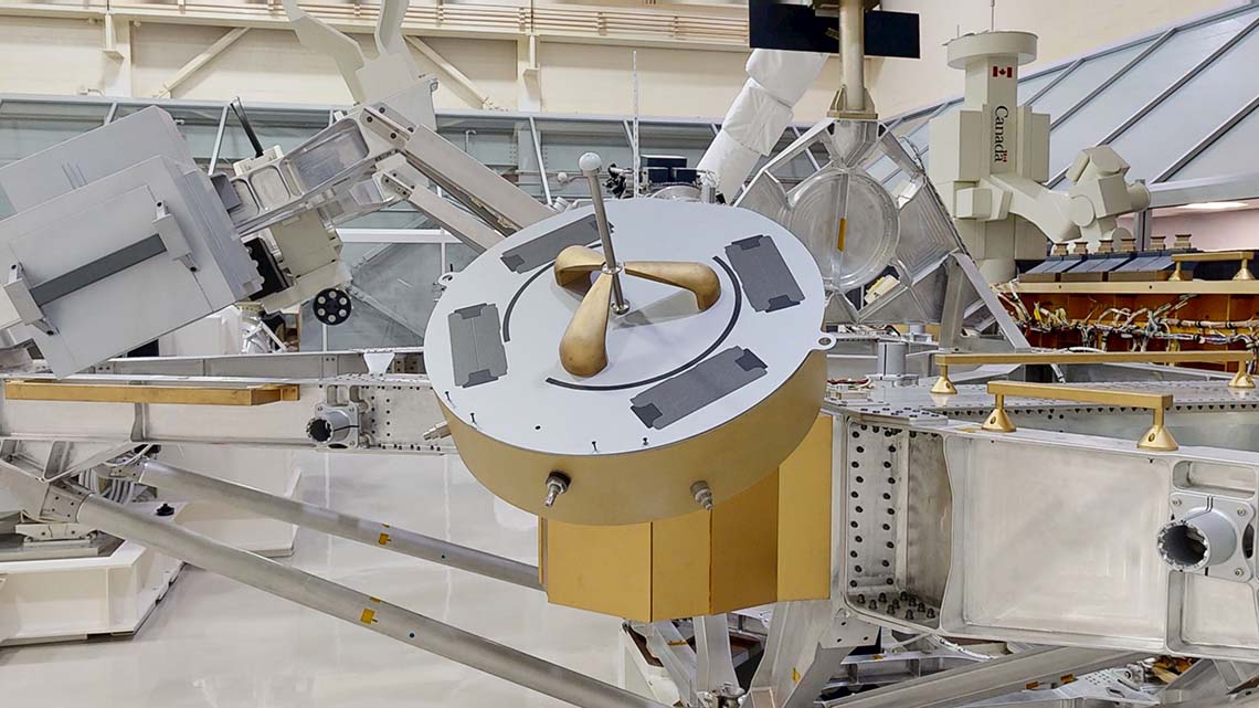 Composant circulaire en métal, avec trois grappins autour d'une longue tige au centre.