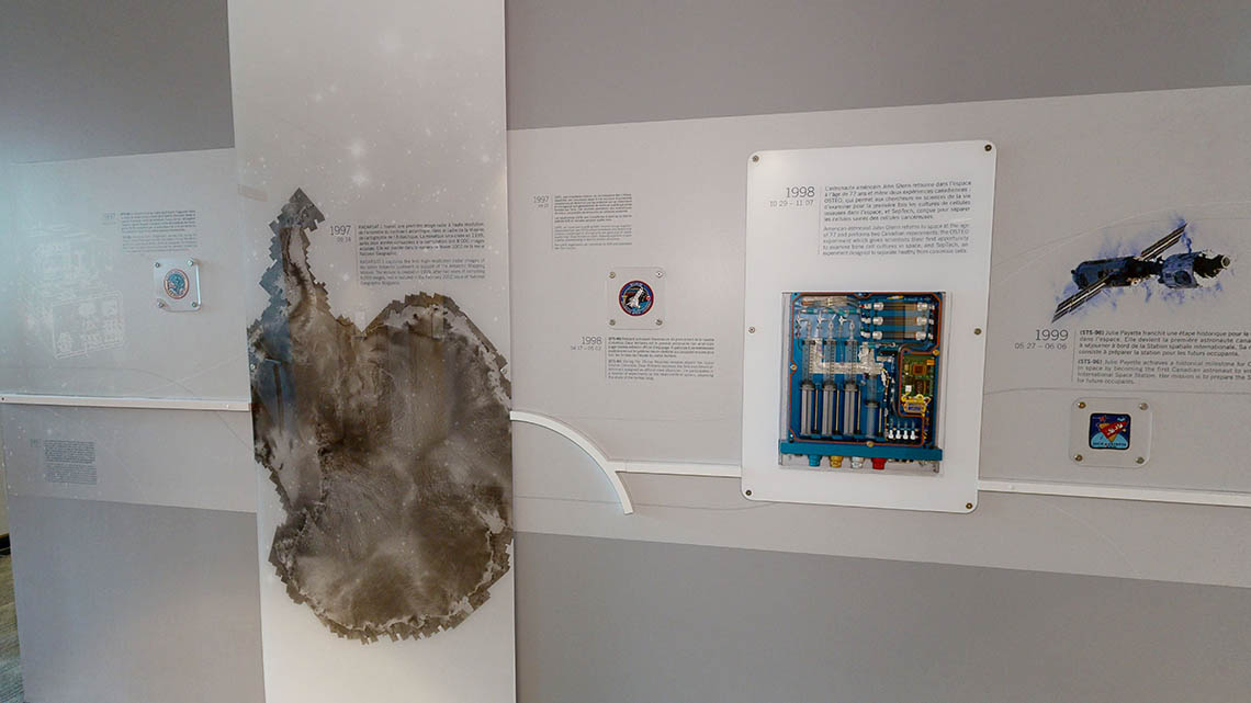 A wall timeline featuring the patches for missions STS-85, STS-90, and STS-96, and a tray used for the OSTEO experiments on the International Space Station.