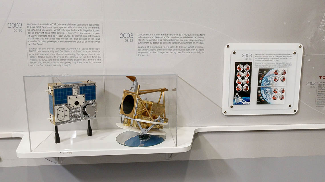 Small models of the MOST and SCISAT satellites. Next to them are a series of stamps mounted on the wall.
