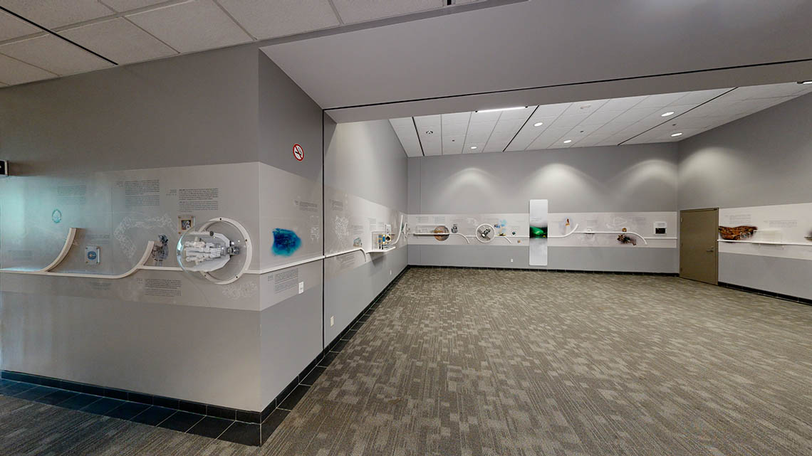 An open area at the Canadian Space Agency conference centre. A timeline composed of text, images, mission patches, and small models runs continuously along the various walls.