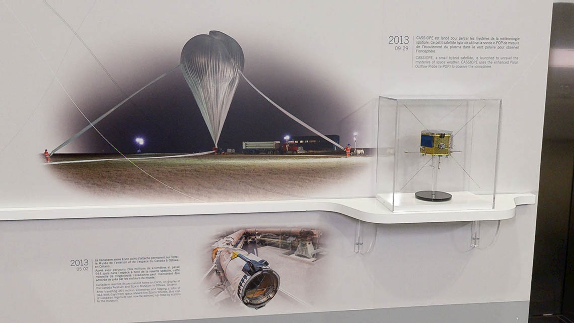 Photos on the wall of a stratospheric balloon and an original Canadarm, and a small model of the CASSIOPE satellite.