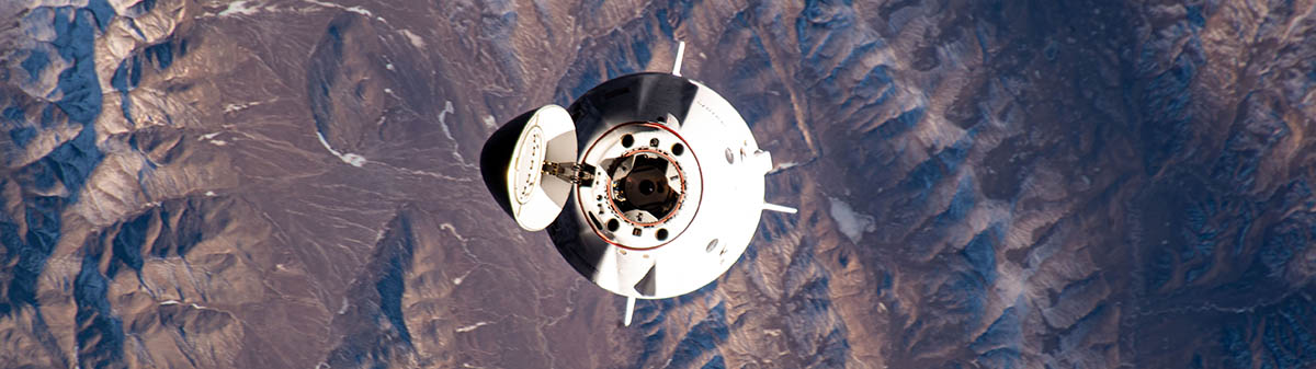 A Crew Dragon capsule in space with mountains in the background.