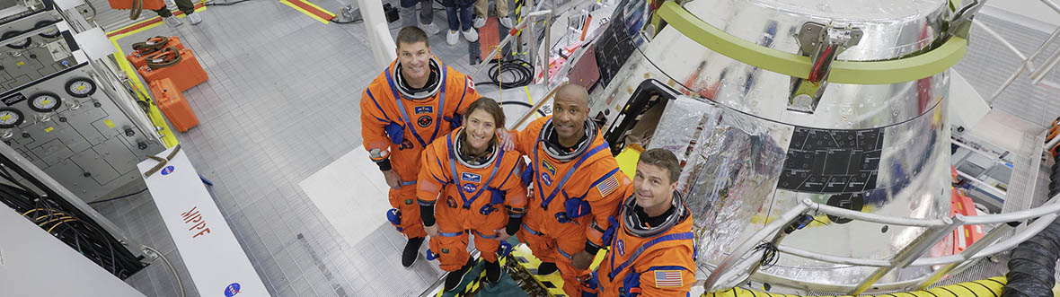 The Artemis II crew in spacesuits in front of the Orion crew module inside a cleanroom.