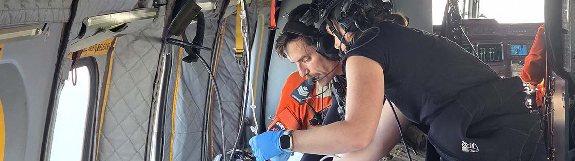 Jenni and a member of 442 Squadron operate medical equipment in a helicopter.