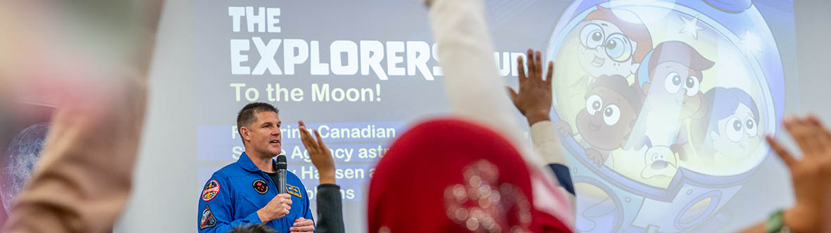 Jeremy talks in a microphone while kids raise their hands to ask him questions.