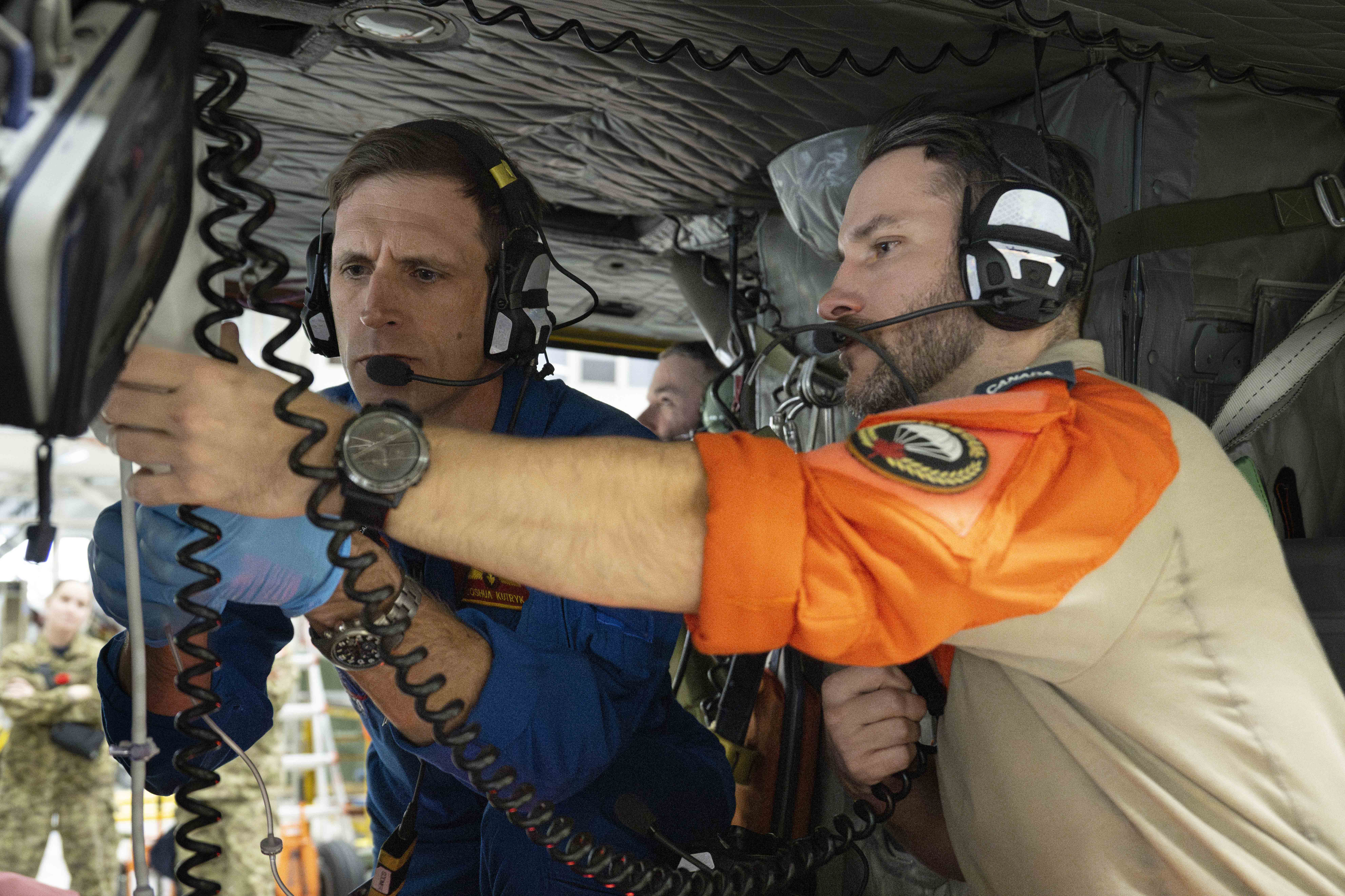 Joshua assists a technician with medical equipment in a helicopter.