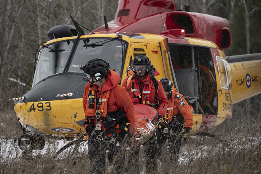 Joshua and a technician carry a stretcher away from a helicopter.