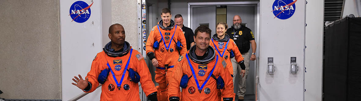 Quatre astronautes sortent du poste d'équipage, suivis de deux gardiens de sécurité.