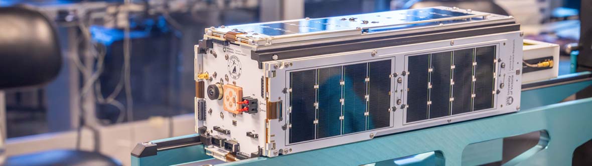 Close-up of a CubeSat equipped with solar panels resting on a support stand in a laboratory
