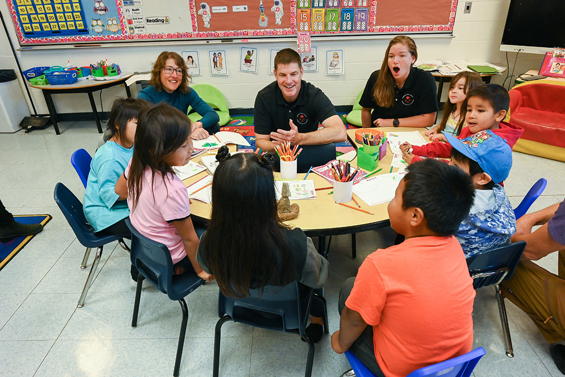 Astronauts sit around a low table with seven young Innu, sharing a laugh.