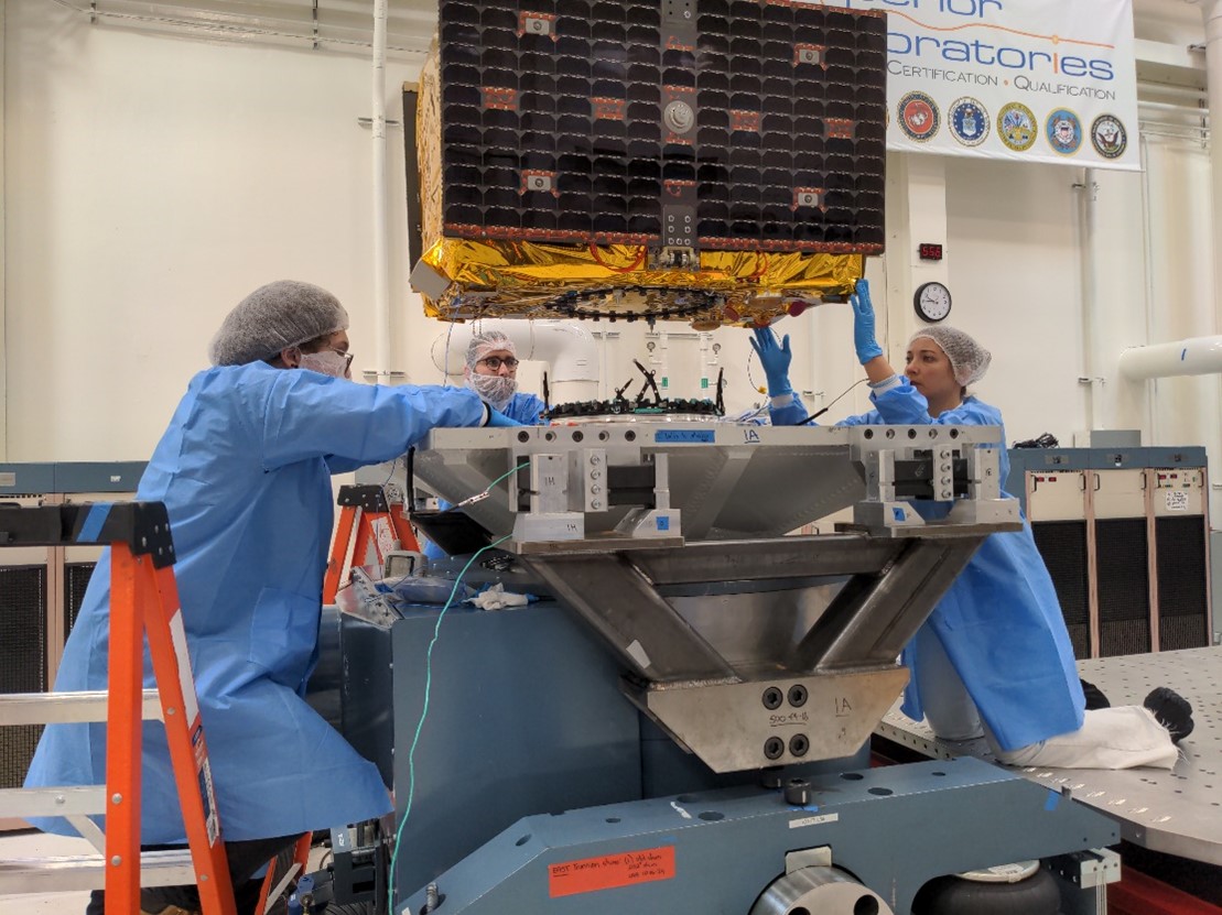 Engineers carefully guide a satellite as it lowers onto the platform of a large machine.