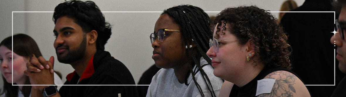 Students in the foreground listening attentively with other students in the back.