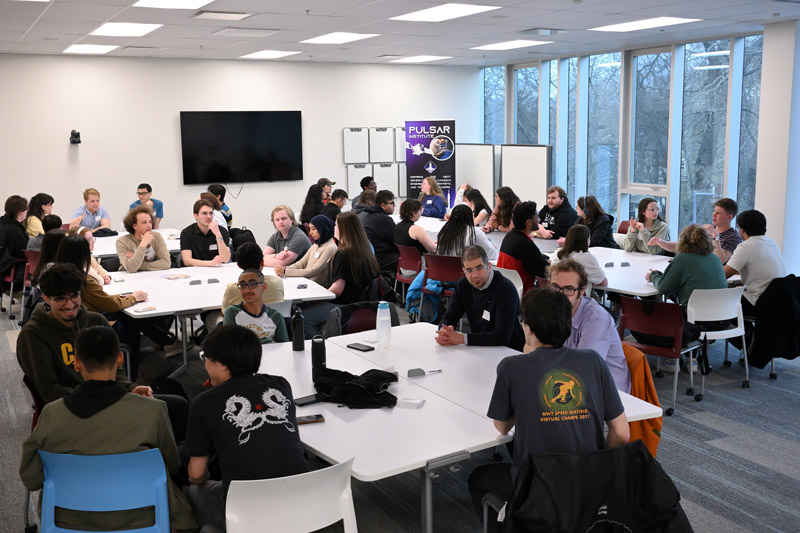 Students seated in groups around tables in a room.
