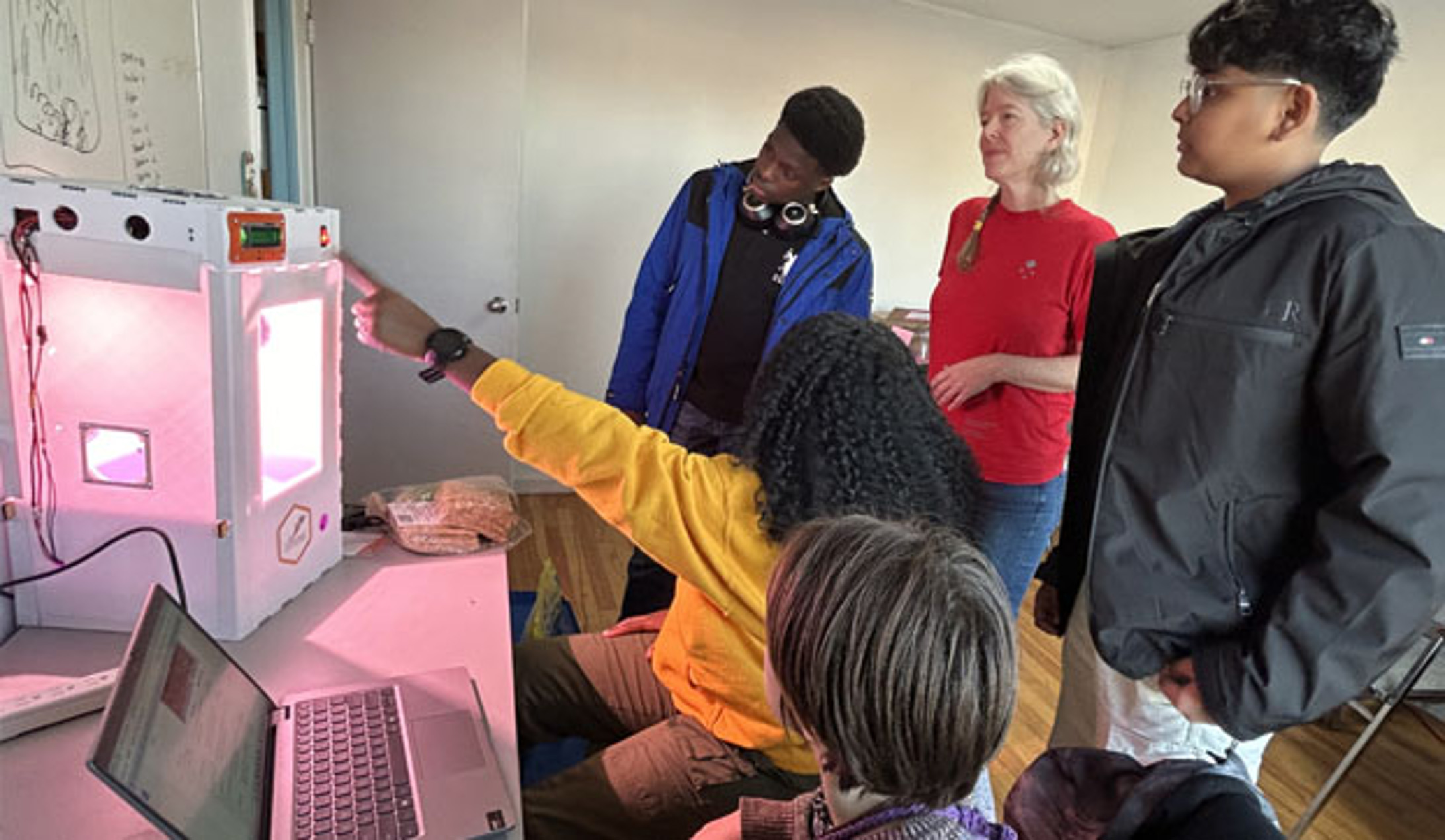 Janice and four teenagers look at a lit box connected to a laptop.