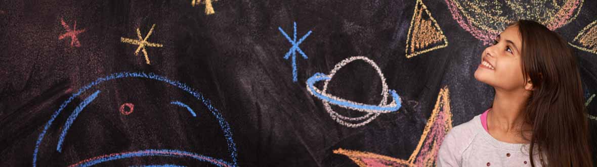 A pre-teen girl smiles at stars and planets drawn in chalk on a blackboard