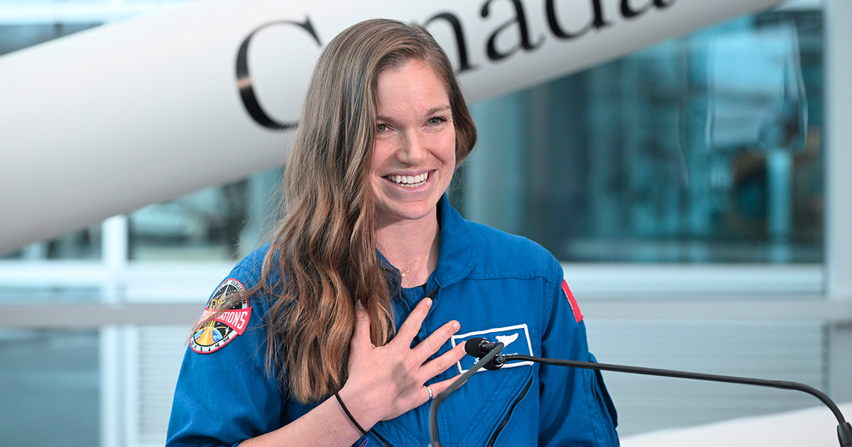 Jenni Gibbons in a blue flight suit speaks at a podium