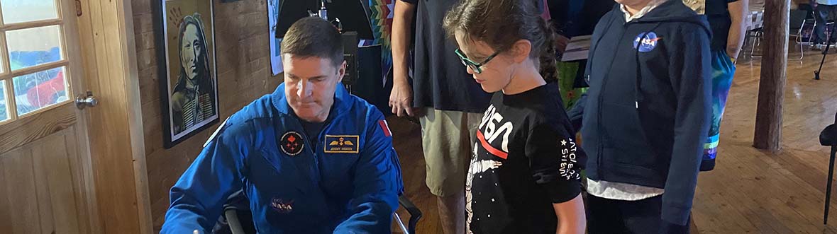 Jeremy signs a poster as children and adults from an Indigenous community look on.