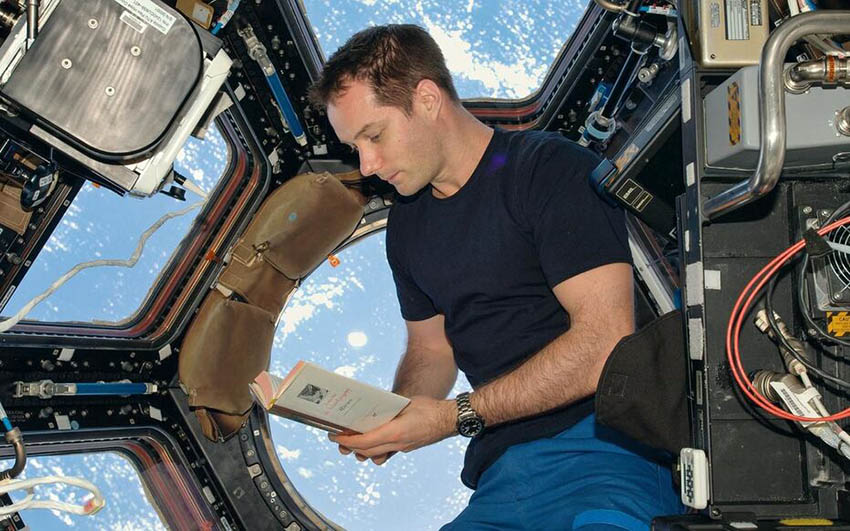 Thomas Pesquet tient un livre. Il est dans la coupole de la Station.