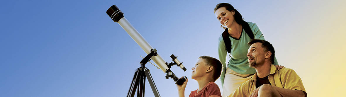 A boy is setting up to look through a telescope, his parents next to him.