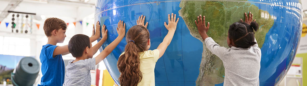 Deux garçons et deux fillettes posent leurs mains sur un globe terrestre géant.