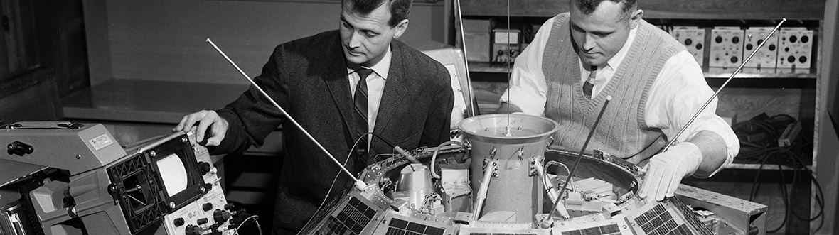 Black and white photo of two men sitting behind the satellite.