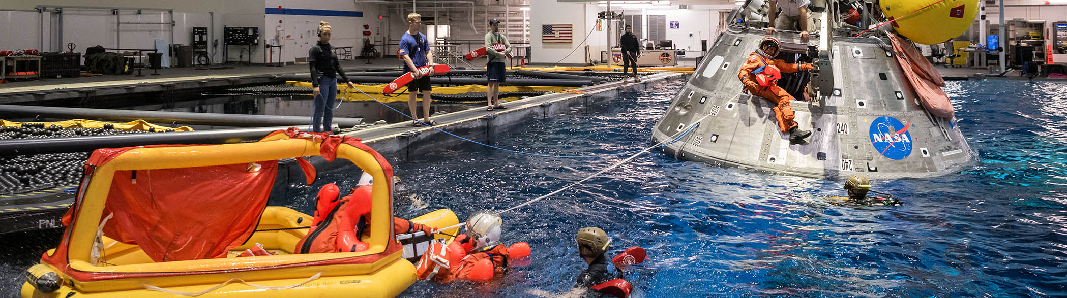 Plusieurs personnes font un exercice d'évacuation d'une capsule spatiale dans une immense piscine intérieure.