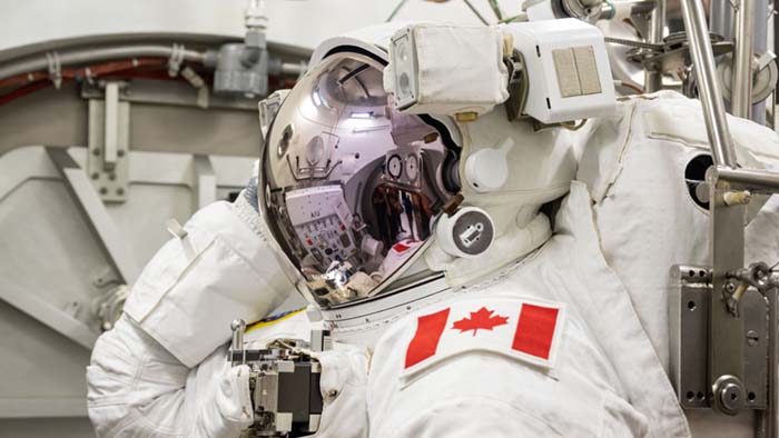 Joshua portant sa combinaison spatiale et son casque. La visière pare-soleil est abaissée