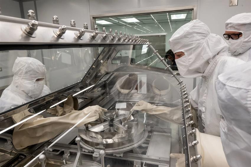 Three people dressed in full-body protective suits practise opening the sample canister, which is inside a glove box.