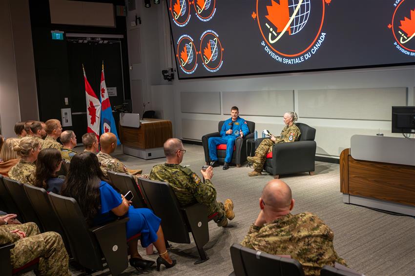 Jeremy prend la parole dans une petite salle de conférences. Certains membres du public portent l'uniforme.