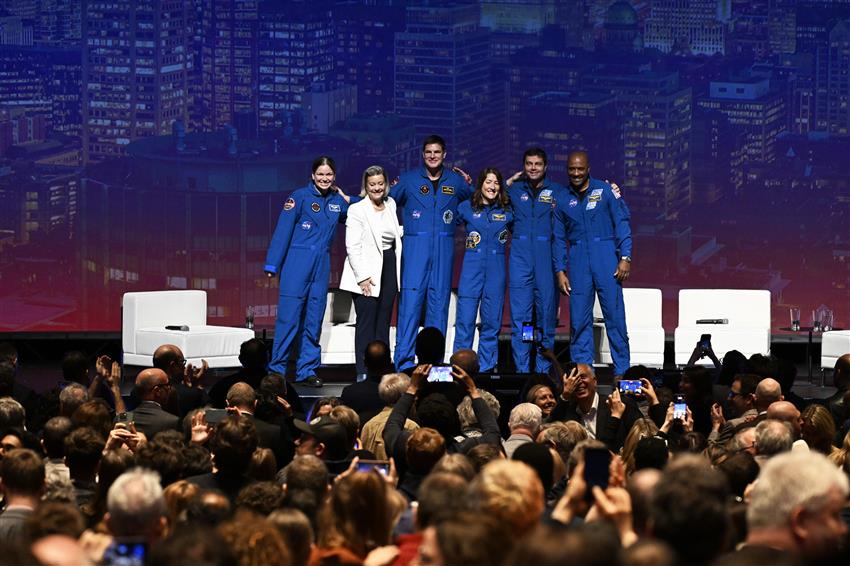 Group photo of the five astronauts and Isabelle on a stage, with a packed audience in front of them.