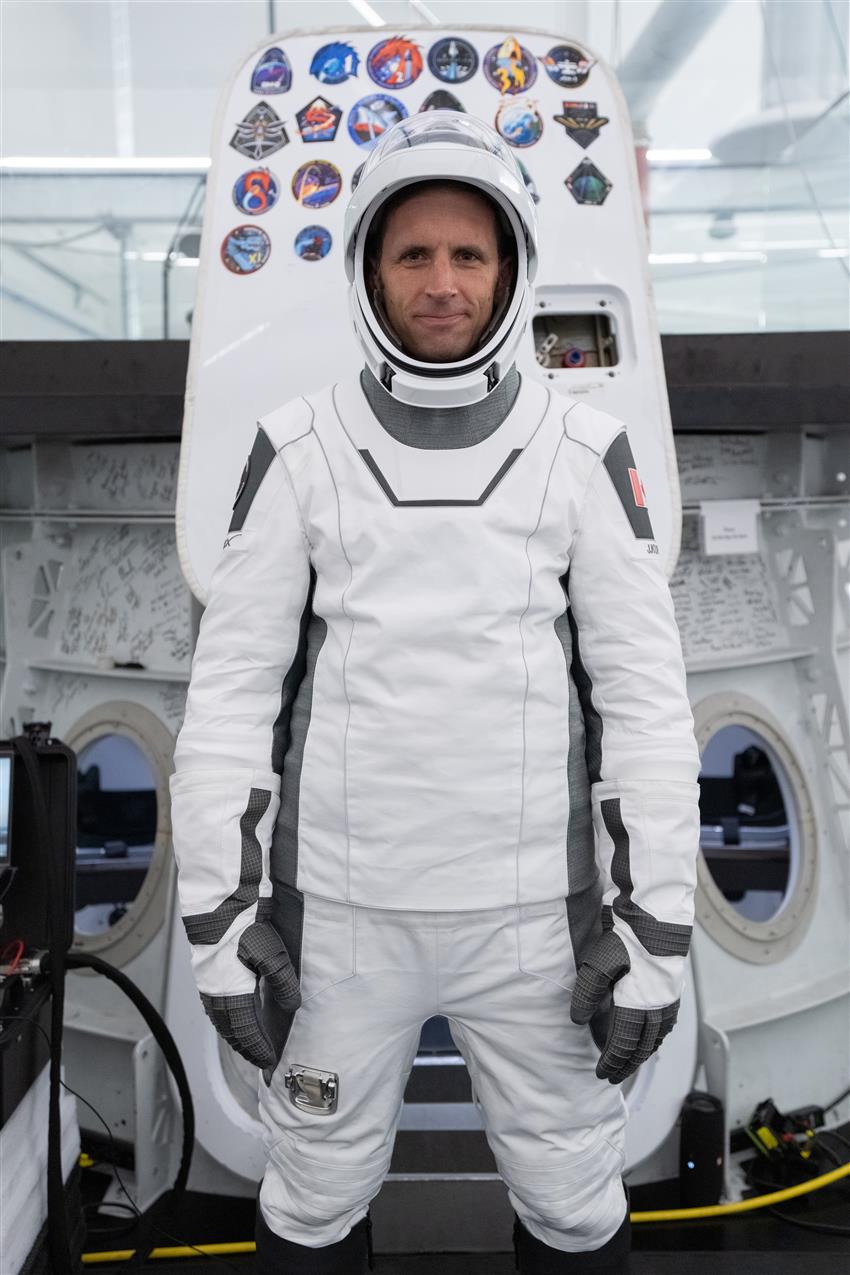 Gros plan de Joshua vêtu d'une combinaison spatiale de SpaceX devant une maquette de capsule spatiale Dragon. 