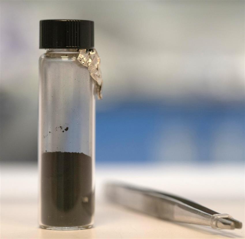 A vial with a small portion of asteroid inside, with tweezers laying to the right. 