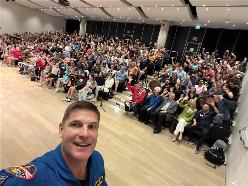 Jeremy se prend en photo. Derrière lui, une salle de conférences bondée.
