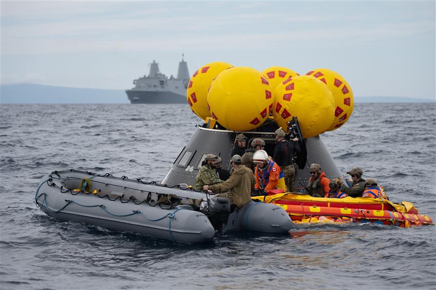 Deux bateaux pneumatiques transportant des gens flottent devant une maquette de vaisseau spatial.