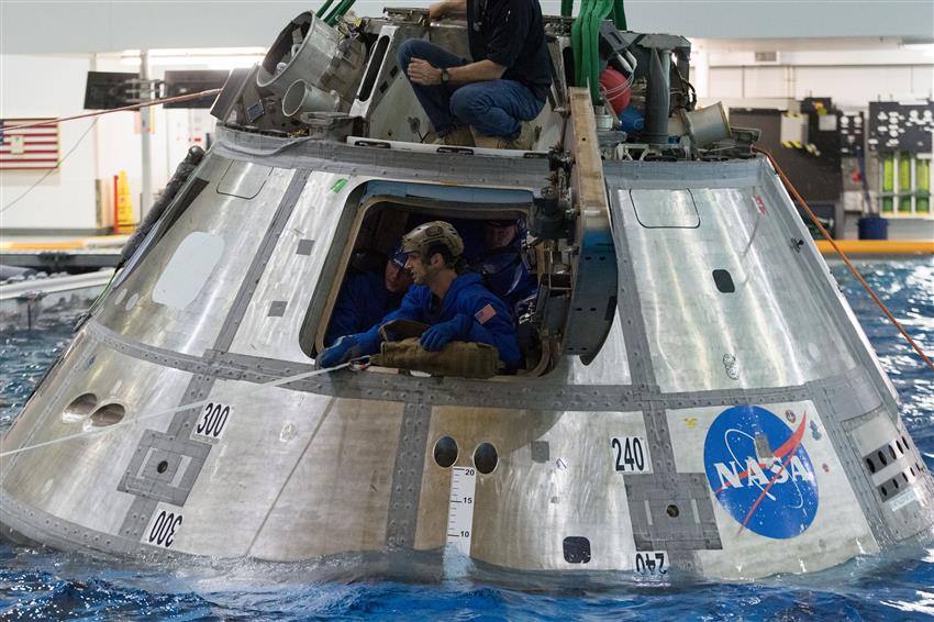 Joshua dans une capsule spatiale dans une piscine s'apprête à sortir par l'écoutille.