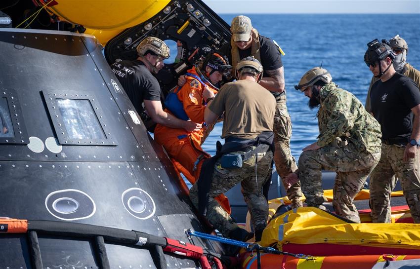 Jenni sort de la maquette d'Orion et des militaires l'aident à monter à bord d'un bateau pneumatique.