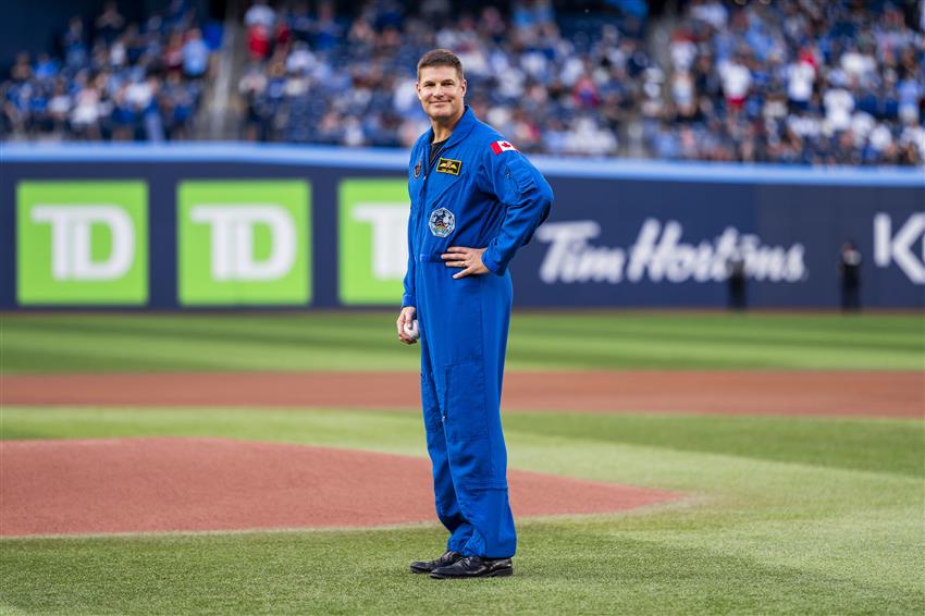 Jeremy en combinaison de vol sur un terrain de baseball, une balle à la main. 