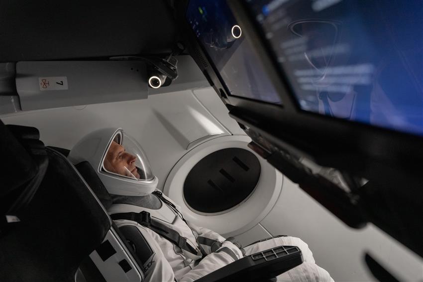 Joshua, vêtu de sa combinaison spatiale, est dans le siège incliné d'une maquette d'une capsule spatiale Dragon.