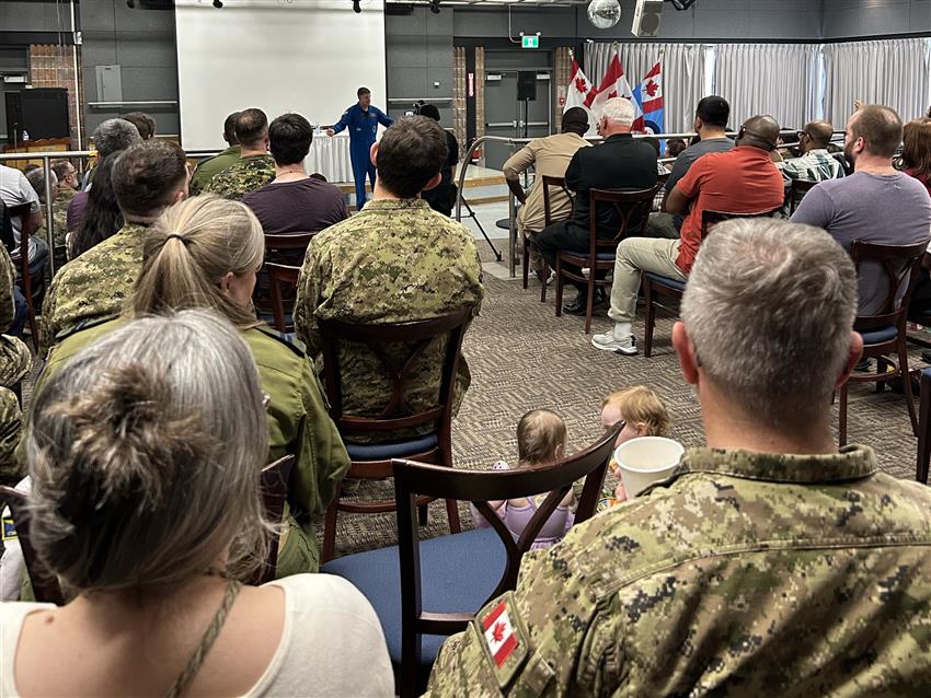 Jeremy prend la parole dans une petite salle de conférences. Certains membres du public portent l'uniforme.