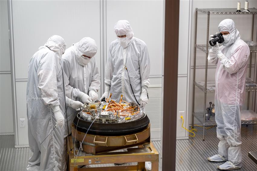 People dressed in protective suits are disassembling a space capsule.