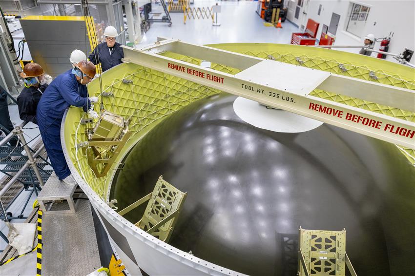 A technician installs a CubeSat in a large ring structure in an assembly building.