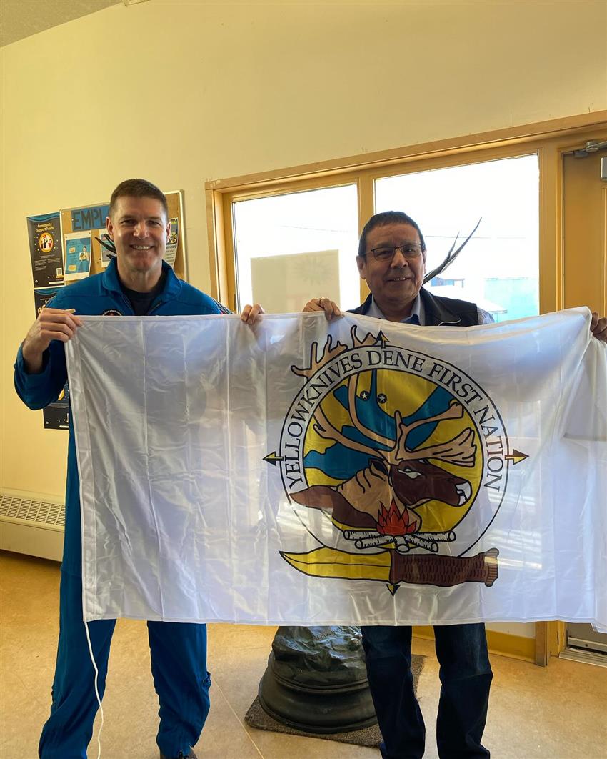 Jeremy pose avec le chef Betsina. Ils tiennent un drapeau de la Première nation des Dénés Yellowknives.