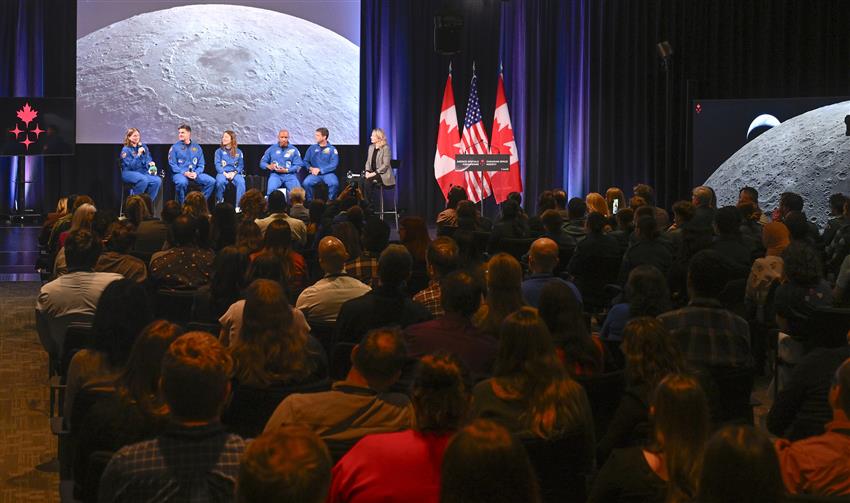 The minister speaks with the astronauts in front of a full audience.