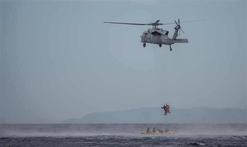 Un astronaute est héliporté, tandis que quatre autres personnes attendent en bas dans un bateau pneumatique.