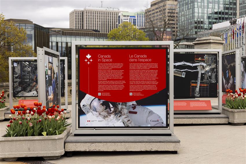 Panneaux informatifs avec images d'astronautes et de technologie spatiale, installée sur une place urbaine.