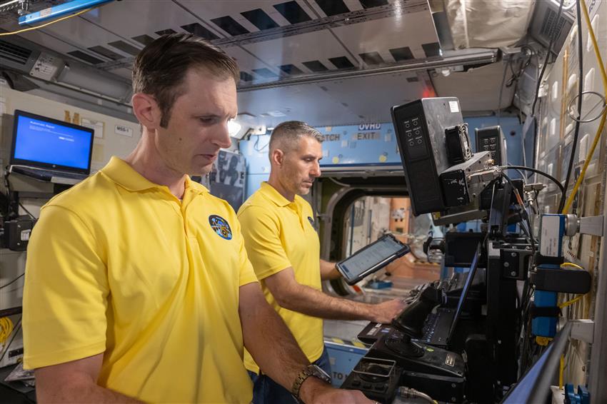 Joshua and Luke standing at a workstation inside a mock-up of the International Space Station. 