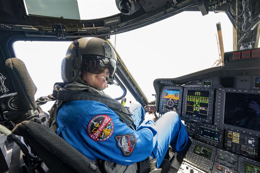 Jeremy dans la cabine de pilotage d'un hélicoptère, le manche à balai dans la main et un casque de pilote sur la tête.