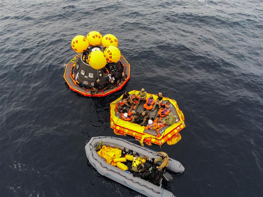 Une douzaine de personnes sur deux bateaux pneumatiques et d'une maquette de vaisseau spatial flottant sur l'océan.