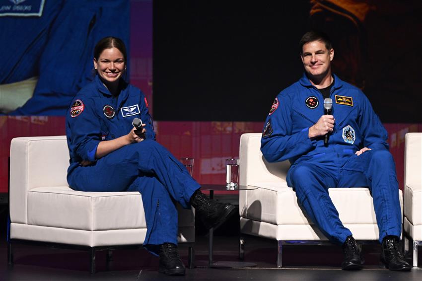 Jenni and Jeremy on stage, holding microphones and smiling.